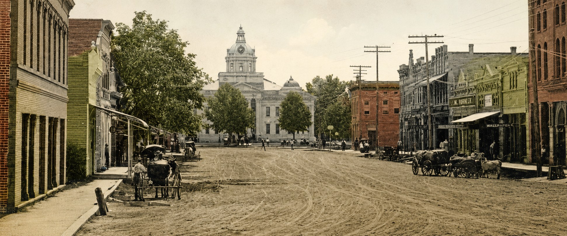 Hand-tinted photograph of Main Street, Columbia, looking toward the 1905 Marion County courthouse — a dirt street with horse-drawn wagons and oxen teams. Photograph courtesy of the Marion County Historical Society.